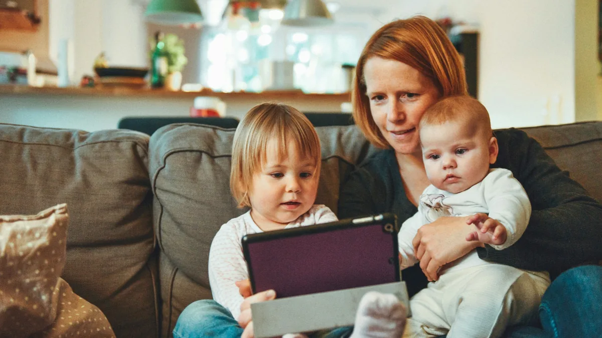 Parent with two young children on a sofa at home, representing dependents to cover