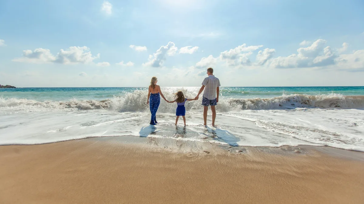 Family of three holding hands on a beach, illustrating who life insurance protects